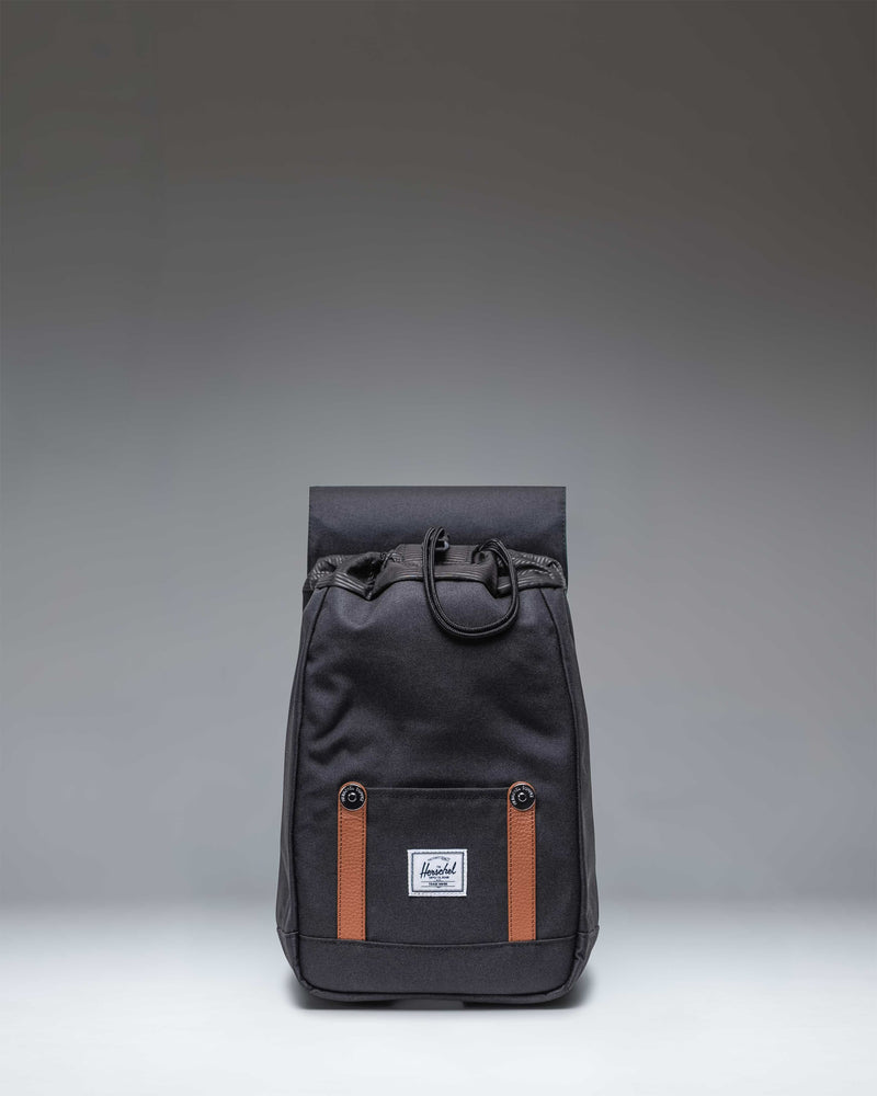 Herschel Supply Co. Retreat Mini Backpack in black, featuring a compact design with a front storage sleeve and magnetic buckle closure straps.