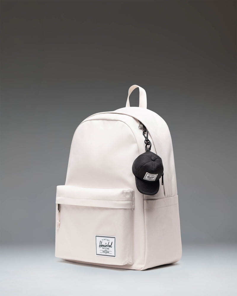Herschel Supply Co Sylas Classic Cap Bag Charm in black, showing the detailed side view of the miniature cap accessory attached to a clip.