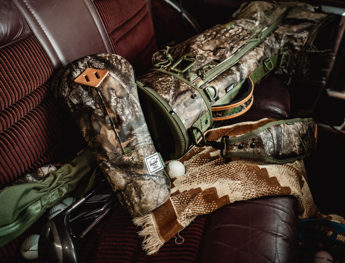 Herschel Supply Co. x Realtree Herschel Heritage Driver Head Cover in the Realtree APX Camo pattern displayed as a hero image.